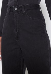 Svarta denimjeans med hög midja. Har en framzipper, metallknapp och sidofickor. Slät yta med subtila urtvättning detaljer.