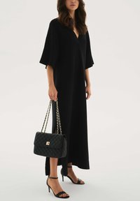 Must, lahtise lõikega kleit V-kaelusega ja lühikeste varrukatega, mida on kombineeritud musta tikk-käekoti ja mustade paeltega kõrgete kontsadega sandaalidega.