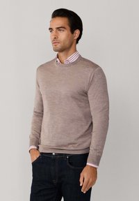Beige coltrui met een subtiele textuur, gedragen over een gestreepte overhemd met kraag. Donkerblauwe spijkerbroek complementeren de outfit.
