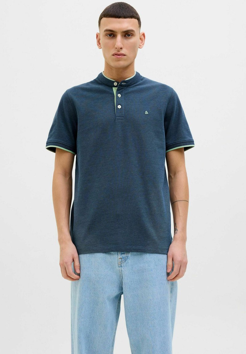 Marineblaues Poloshirt mit kurzen Ärmeln, Knopfleiste, kontrastierendem hellgrünem Kragen und Bündchen. Weicher Stoff mit einer subtilen Textur.