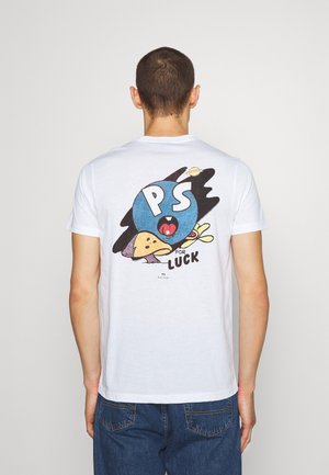 Persoon die een wit T-shirt draagt met een kleurrijke afbeelding van een blauwe cirkel, een paddenstoel en de tekst "PS for luck" op de achterkant, gecombineerd met een blauwe spijkerbroek.