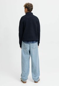 Navy pullover met hoge kraag, gecombineerd met lichtblauwe oversized jeans. Zacht textuur en casual pasvorm. Subtiele stikdetails zichtbaar.