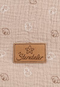 Beige, strukturierter Stoff mit weißen und braunen Schafmustern; verfügt über ein genähtes braunes Lederetikett mit "Stern-taler" Branding.