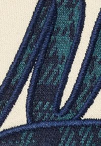 Diseño bordado que presenta hilos verdes y azul marino sobre tela crema, representando hojas estilizadas con texturas y formas distintas.