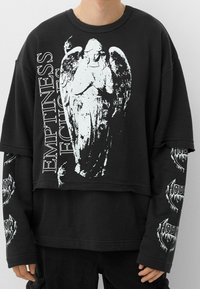 Černá oversized mikina s bílou grafikou anděla a textem "PRÁZDNOTA ECHOES." Dlouhé rukávy s tištěnými akcenty. Hladký bavlněný materiál.