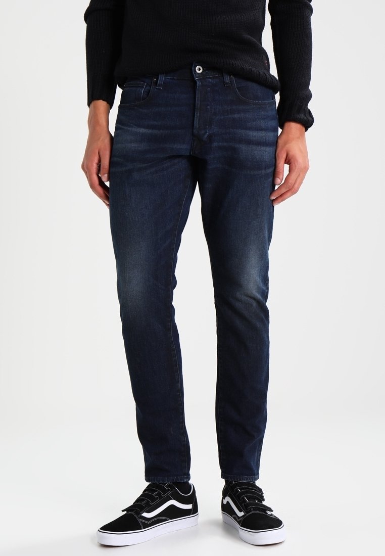 Tmavě modré džíny s úzkým střihem a drobným vyblednutím, doplněné černobílými teniskami s výrazným pruhovaným designem.