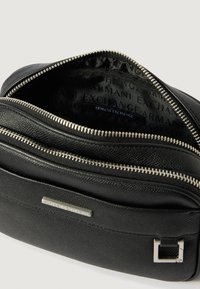Czarna torba z fakturowanej sztucznej skóry z srebrnym okuciem, podwójnymi zamkami błyskawicznymi i wnętrzem oznaczonym "ARMANI EXCHANGE."