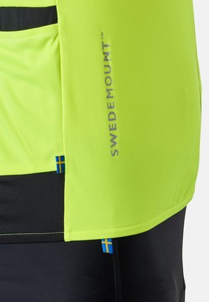 Neongeel en zwart kledingstuk met "Swedemount" logo en kleine Zweedse vlaglabels op de binnennaden, met zichtbare stoftextuur en stikwerkdetails.