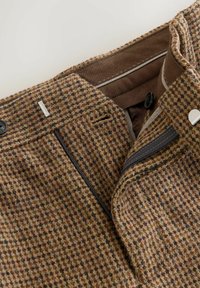 Brown check-patterned trousers made from textured fabric. Features include a button closure, zip pockets, and contrast lining.