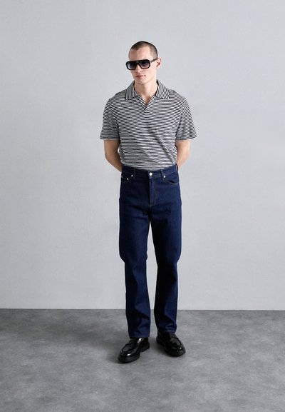 Polo à manches courtes rayé en noir et blanc, associé à un jean en denim bleu foncé et des mocassins noirs. Design minimaliste avec une coupe classique.