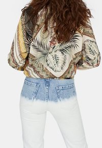 Patroonblouse in beige, groen en gele tinten, gecombineerd met witte jeans met een blauw ombre-effect bij de taille.