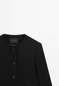 Manteau noir à manches longues avec encolure ronde et trois boutons sur le devant, présenté de la poitrine vers le haut sur un fond blanc.