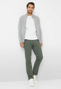 Grijze gebreide zip-up cardigan over een wit T-shirt, gecombineerd met groene broek en witte sneakers. Het design is casual en aansluitend.