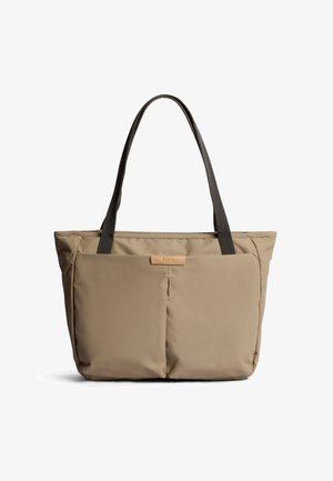 Sac cabas beige avec deux poches avant et poignées foncées, design minimaliste adapté à un usage quotidien ou aux voyages.
