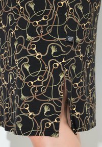 Czarna spódnica z wzorem łańcuchów, kajdanek i zielonych akcentów. Materiał jest gładki, z bocznym rozporkiem i małą metką marki.