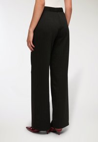 Czarne spodenki wide-leg w prążki z gładką fakturą i elastycznym pasem, w zestawie z burgundowymi butami na spiczastej podeszwie.