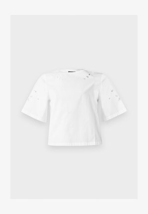 Blouse blanche à manches courtes avec des manches larges et petits motifs décoratifs découpés en forme de feuilles aux épaules et aux manches.