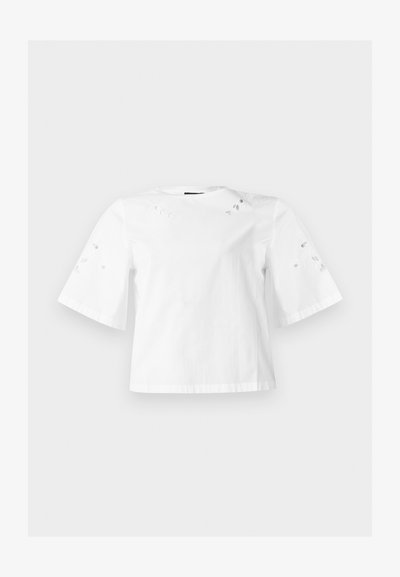 Λευκό μπλουζάκι με κοντά μανίκια και φαρδιά μανίκια με μικρά διακοσμητικά σχέδια φύλλων στους ώμους και τα μανίκια.