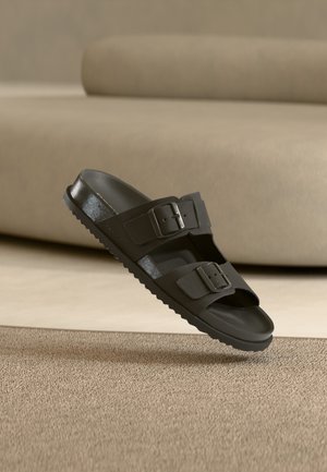Sandali neri a ciabatta con due cinturini regolabili con fibbia, soletta testurizzata e suola rigata, su sfondo neutro.