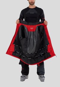 Rød og sort isoleret jakke med lynlås foran, mesh-lommer og justerbare stropper, holdt åben for at vise indvendige detaljer.