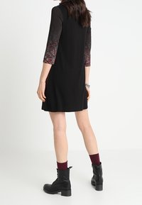 Czarna sukienka z rękawami o długości do połowy przedramienia w paisley, casualowy fason, długość do połowy uda, zestawiona z czarnymi botkami na sznurowadła i bordowymi skarpetkami.