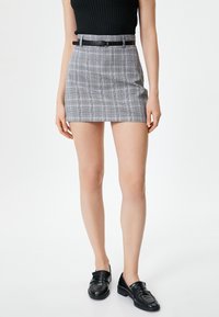 Grau karierte Minirock mit taillierter Passform, einem schwarzen Gürtel und glatter Textur, kombiniert mit schwarzen Loafern und einem gerippten schwarzen Oberteil.