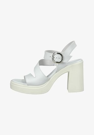 Sandale blanche à talon haut avec talon épais, larges brides croisées et bride de cheville à boucle argentée sur une semelle plateforme.