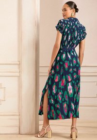Abito blu navy a maniche corte con vivaci macchie rosa e verde, spacco laterale e vita con cintura. Indossato con sandali con tacco a blocco dorati.