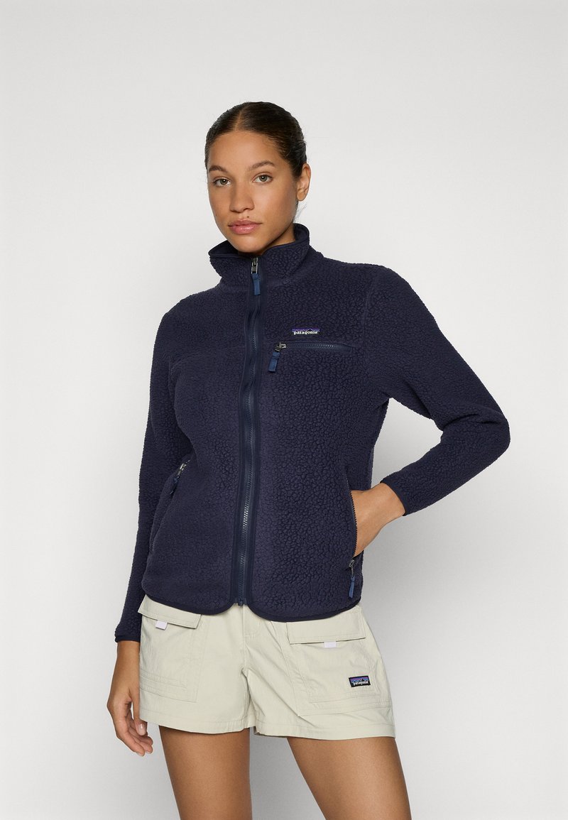Giacca in pile blu navy con colletto alto, zip full-length e due tasche frontali; presenta un materiale morbido e testurizzato e il logo Patagonia sul petto.