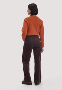 Oranje gebreide trui met raglanmouwen, gecombineerd met donkerpaarse ribfluweelbroek. De outfit heeft een ontspannen pasvorm en een gestructureerde stof.