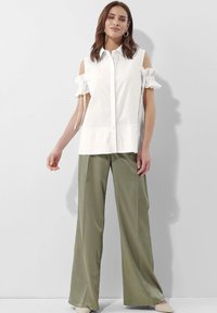 Witte, shirt met korte mouwen en open schouders, met gerimpelde manchetten, gecombineerd met olijfgroene, wijde broek en lichtgekleurde schoenen.