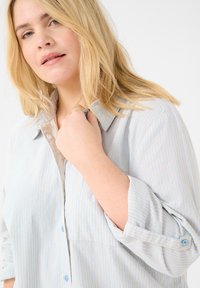 Chemise à boutons bleu clair avec des rayures verticales blanches, dotée d'une texture douce, d'un col, de manches retroussées et de boutons bleu clair.