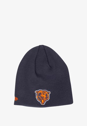 Berretto a maglia blu navy con logo di orso ricamato arancione e bianco sulla parte anteriore, con una cima affusolata e dettagli cuciti lungo i bordi.