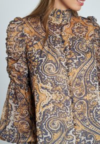 Blusa de manga larga en tejido ligero y con estampado que presenta bold paisley en naranja, azul marino y crema, con mangas abullonadas texturizadas y botones.