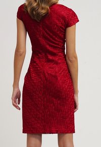 Robe rouge ajustée à manches courtes, en tissu texturé avec un motif ressemblant à des feuilles tissées, longueur genoux et avec une légère brillance.