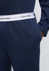Σκούρο μπλε παντελόνι jogging από μαλακό ύφασμα, με λευκή ελαστική μέση που φέρει το λογότυπο 'Calvin Klein' και πλαϊνές τσέπες.