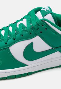 Zelená a bílá Nike teniska s texturovaným koženým svrškem, polstrovaným jazykem a tkaničkami, s výrazným logem a kontrastním prošíváním.