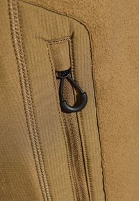 Tan stof met een gladde, textuurafwerking; heeft een rits en een zwarte trekker. Zichtbare stiksels langs de randen.