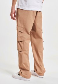 Beige cargobroeken van katoen met zijzakken en een losse pasvorm. Gecombineerd met witte sneakers met zwarte accenten.