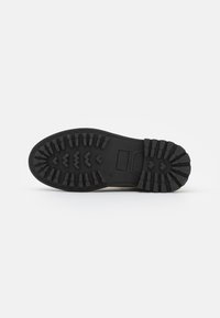 Suela de zapato de goma negra con un patrón de textura que presenta surcos en zigzag y multidireccionales para tracción. Bordes lisos y detalle del logo.