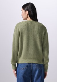 Olivgrön ribbad stickad tröja med långa ärmar och rundad halsringning, kombinerad med ljusblå denimjeans. Texturerad tyg.