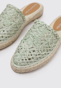 Sandalias de tela verde tipo slipper, hechas de fibras naturales, con un patrón decorativo circular y una suela de yute estilo espadrille.