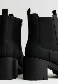 Svarta ankelstövlar med matt yta, med en kraftig klack, elastiska sidopaneler och en dragkedjedetalj på ena sidan.