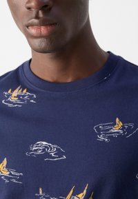 T-shirt blu navy in cotone con scollatura rotonda, caratterizzato da un design di barche gialle e onde ricamate sul tessuto.