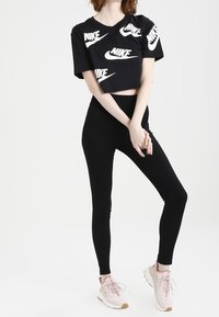 Svart kortärmad T-shirt med vita Nike-logotyper, tillsammans med svarta leggings och ljusrosa sneakers. Outfiten visar en avslappnad, sportig stil.