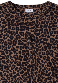 Blouse marron avec imprimé léopard noir et brun foncé, encolure ronde et trois boutons noirs sous le col.
