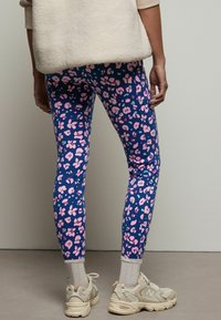 Leggings hebben een blauwe achtergrond met roze bloem- en abstracte patronen. Gepaard met crèmekleurige sokken en lichtgekleurde sneakers.