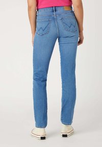 Jeans ajustados de denim azul claro. Cuentan con una cintura alta, bolsillos traseros con un diseño en zigzag y un parche de cuero con el logo.