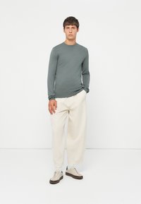 Green long-sleeve fitted top, cream wide-leg pants, and beige sneakers with dark accents. Smooth fabric, relaxed fit, and minimal design.