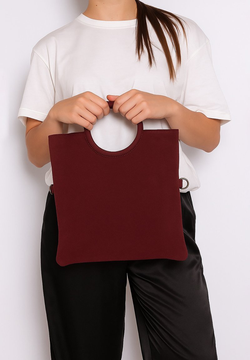 Borsa a spalla bordeaux con manico circolare, texture morbida e forma rettangolare minimalista. Indossata da una persona con una maglietta bianca e pantaloni neri.